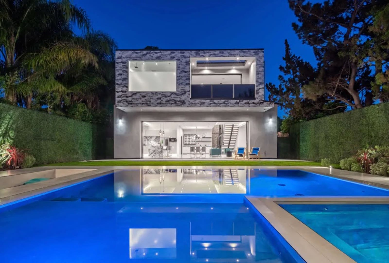 Lit pool in front of a two-story modern house at night